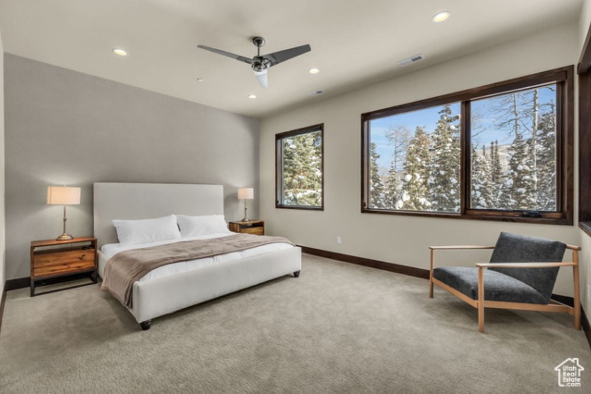 A bedroom with a bed, nightstand, lampshade, chair, ceiling fan, and window.