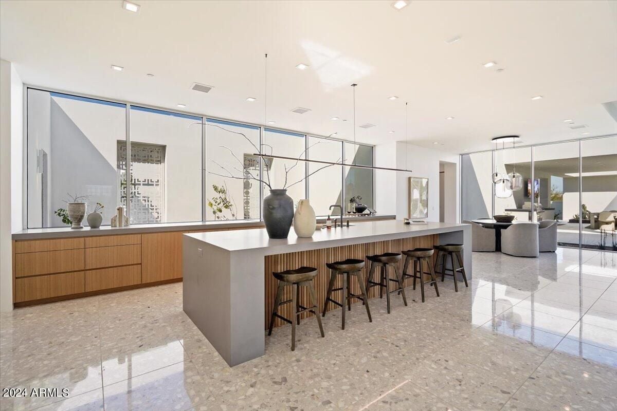 A kitchen with a tiled floor, white ceiling, island, chairs, and wooden cabinets.