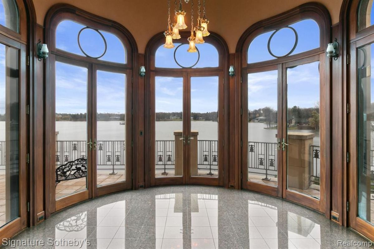 A sunroom with windows, a chandelier, and a tiled floor.