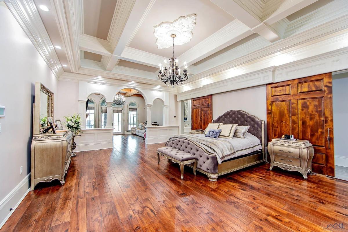 Bedroom with a large bed, chandelier and a wooden floor.