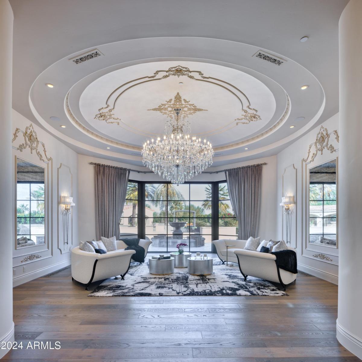 Living room with couches, glass walls, wooden floor and a chandelier.
