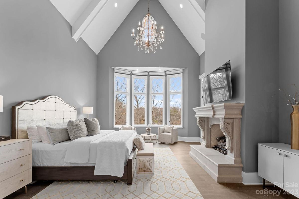 Bedroom with a large bed, chandelier, fireplace and a wooden floor.