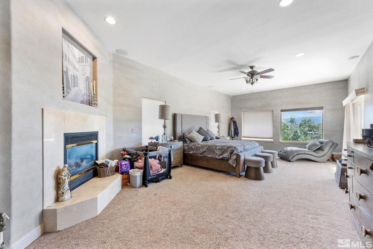 Bedroom with a large bed, fireplace, ceiling fan, and carpet flooring.