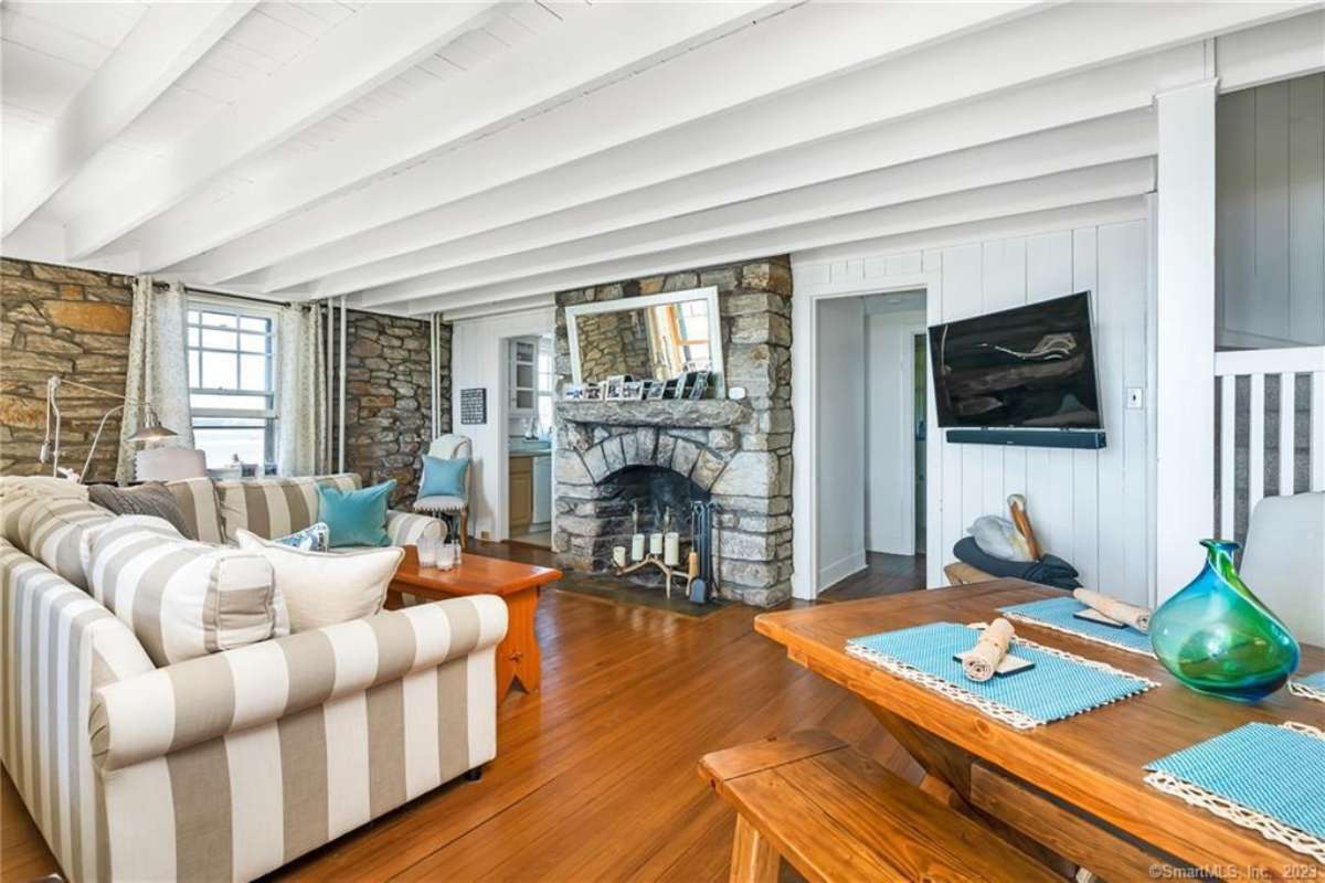 A family room with a fireplace, wooden floor, exposed beam ceiling, a couch, a coffee table, and a TV.