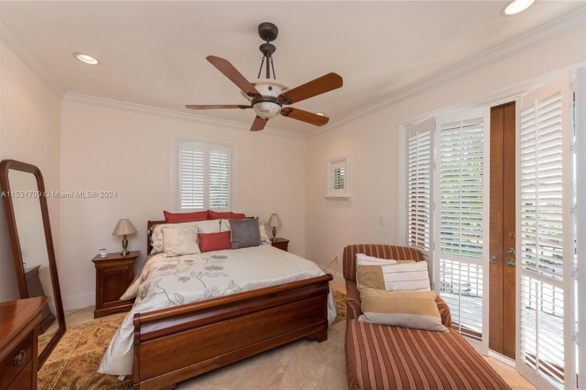 A bedroom with a mirror, bed, nightstand, lampshade, windows, a white ceiling, and a ceiling fan.