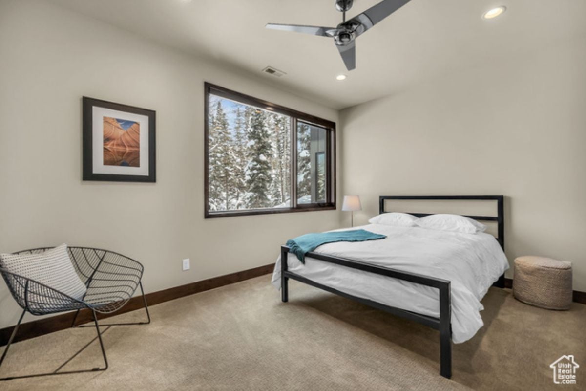 A bedroom with a bed, chair, ceiling fan, and window.