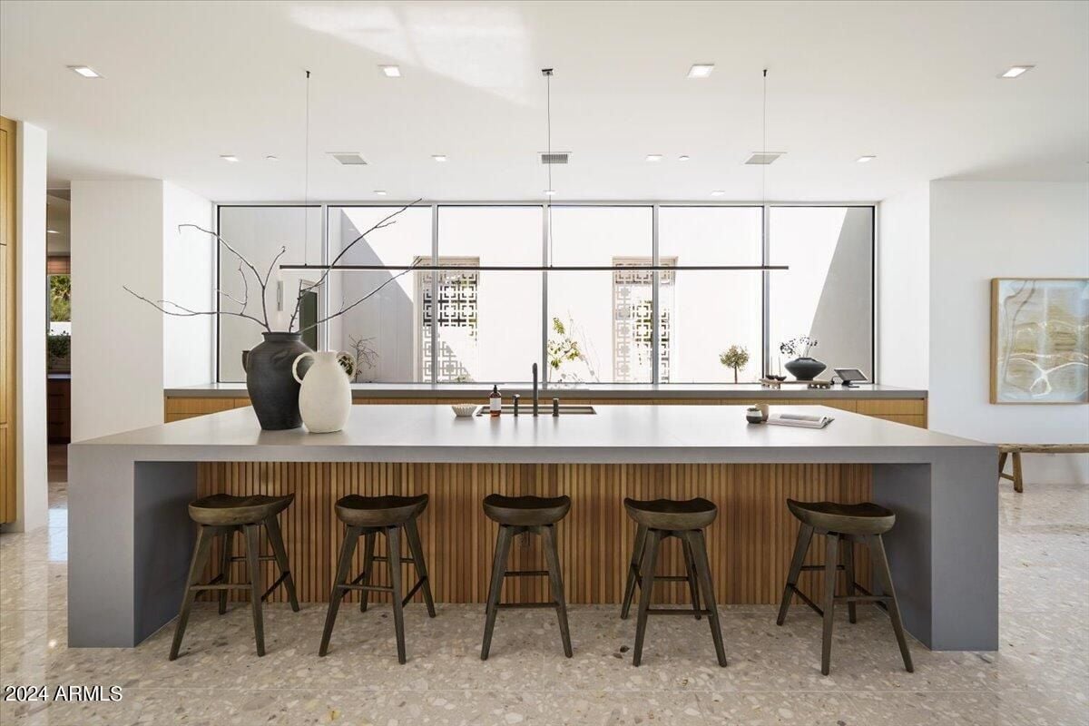 A kitchen with a tiled floor, white ceiling, island, chairs, and wooden cabinets.