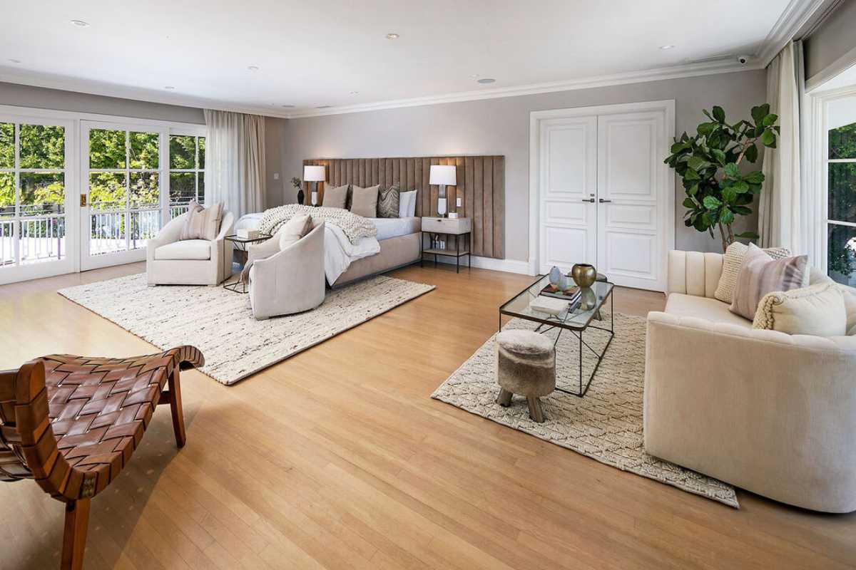 A bedroom with a bed, rug, wooden floor, nightstand, couch, chairs, windows, coffee table, and a white ceiling.