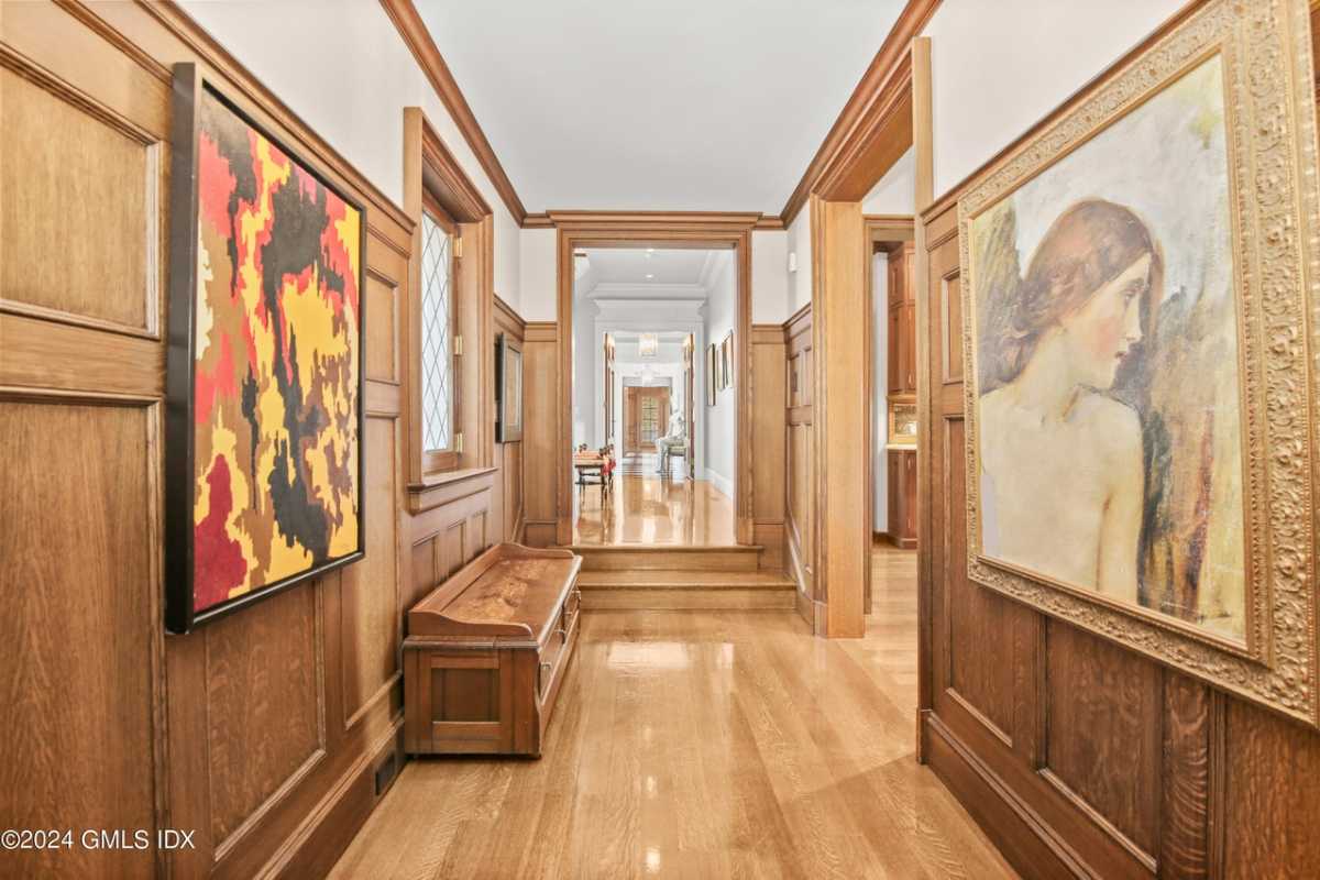 A hallway with a wooden floor, wooden walls, a white ceiling, paintings, and a wooden bench.