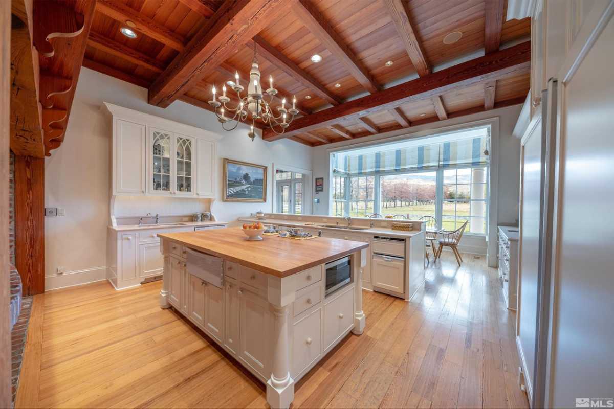 A kitchen with wooden floors, an exposed beam ceiling, an island, and a chandelier.