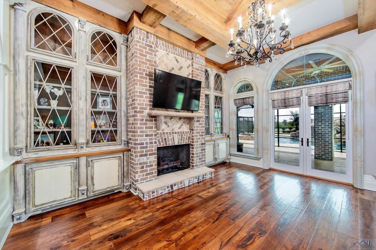 Living room with glass windows, wooden floor, TV and a fireplace.