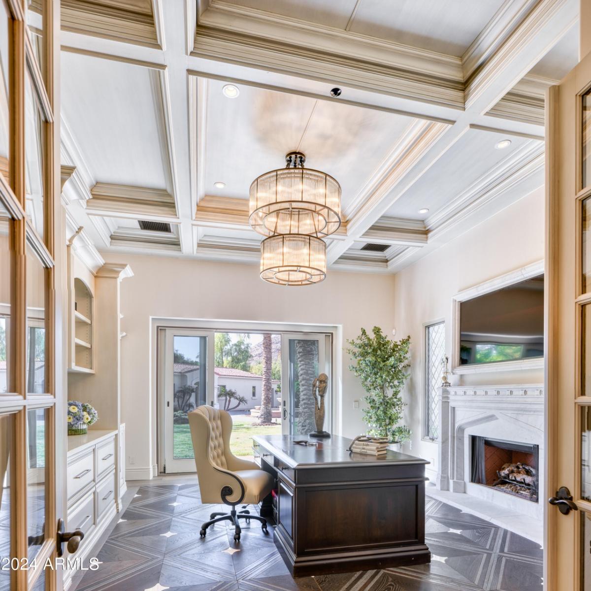 Home office with a desk, chair, chandelier, fireplace and glass doors.