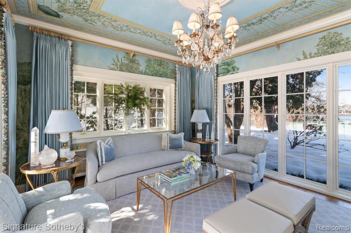 Living room with a couch, chandelier, chairs, table and glass walls.