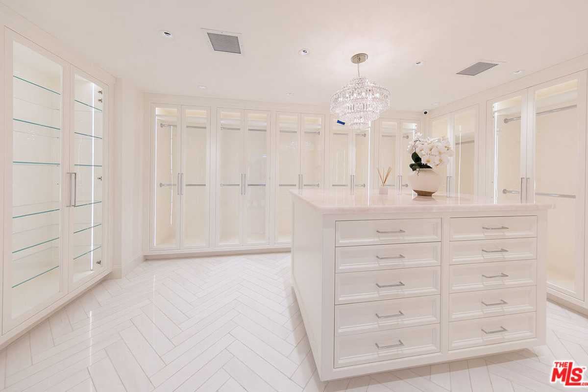 A walk-in closet with a tiled floor, white ceiling, center island, chandelier, and white cabinets.
