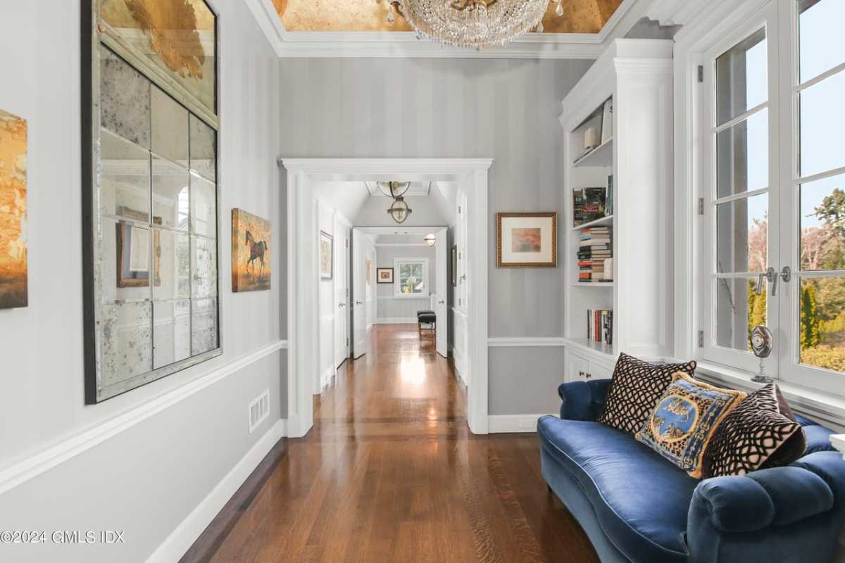 A hallway with a wooden floor, white walls, a window, and a blue couch.