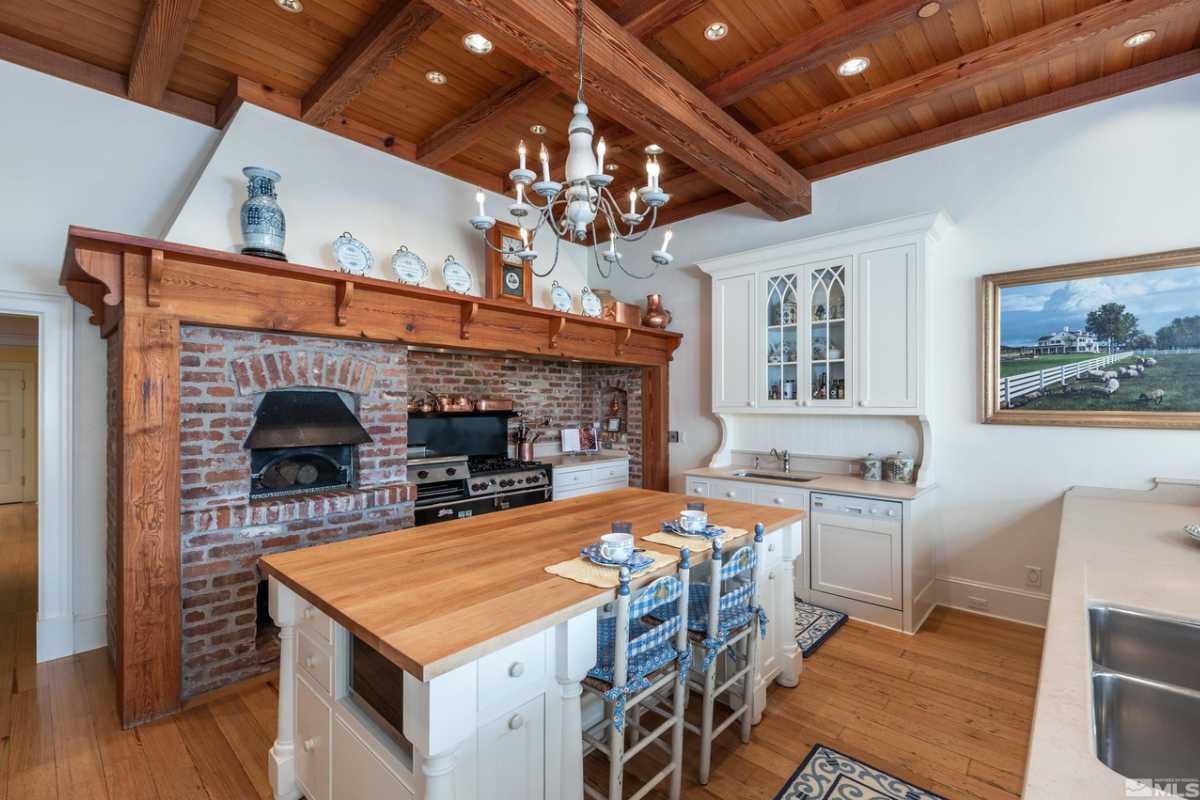 A kitchen with a center island, chairs, a chandelier, an exposed beam ceiling, and a customized oven.