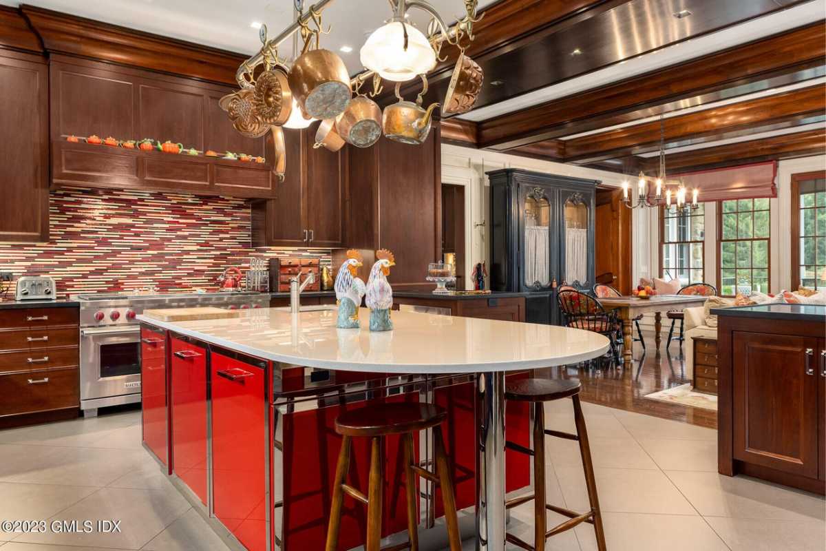 A kitchen with a center island, stools, tiled floor, chandelier, wooden cabinets, and kitchen appliances.