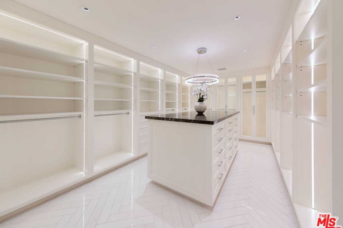 A walk-in closet with a tiled floor, white ceiling, center island, chandelier, and white cabinets.