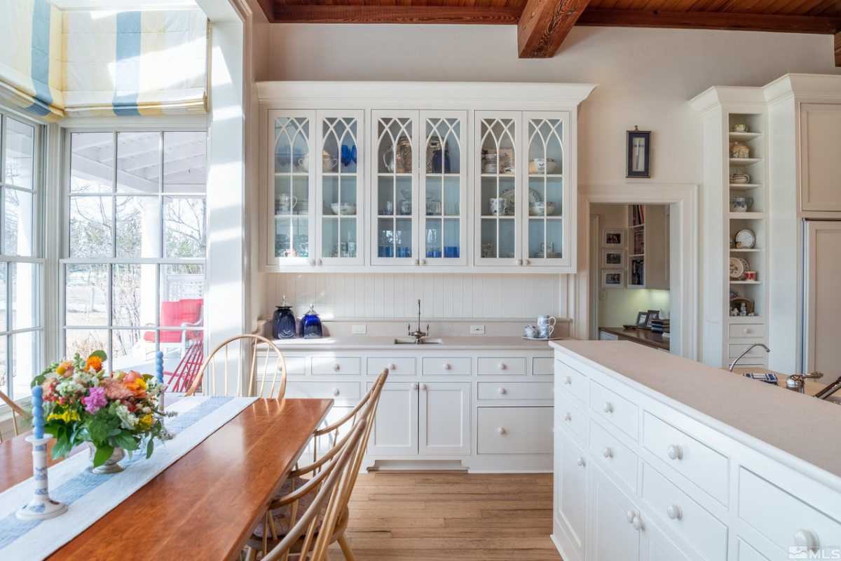 A kitchen with wooden floors, countertops, white cabinets, and a table with chairs.