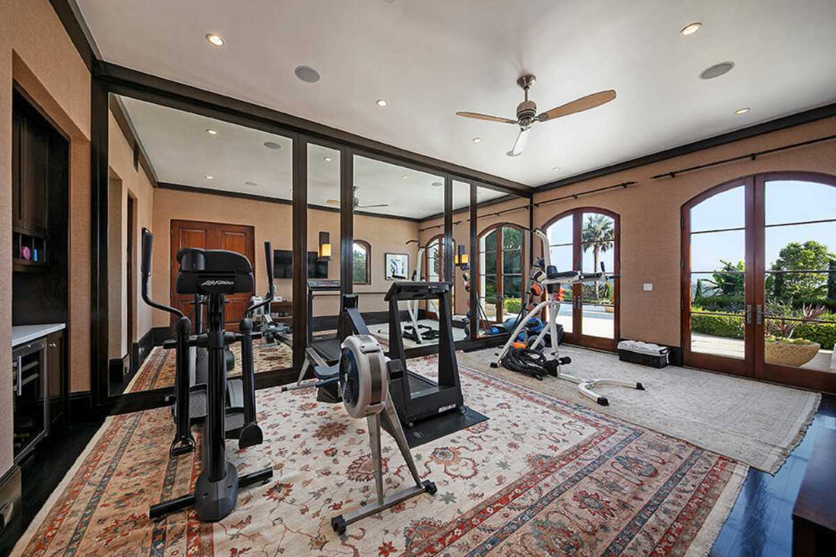 A home gym with a rug, windows, a mirror, a white ceiling, a ceiling fan, and gym equipment.