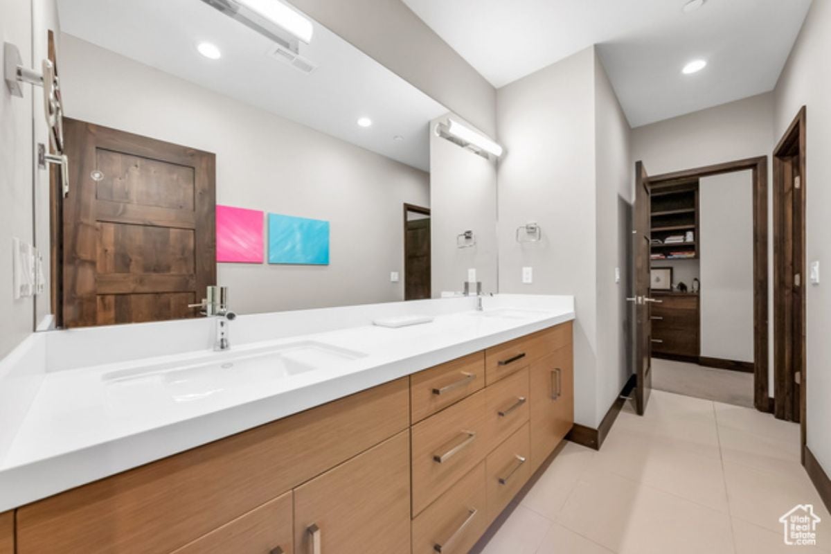 A white bathroom with a large white countertop, a large mirror, sink, and cabinets.