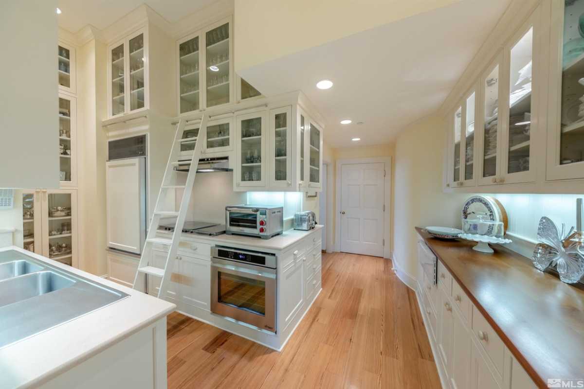 A kitchen with wooden floors, countertops, sink, white ceiling, white cabinets, and kitchen appliances.