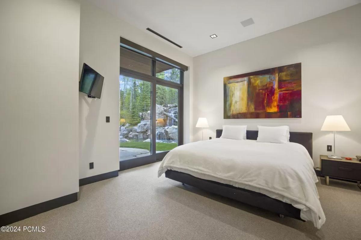 Bedroom with a large bed, glass doors, TV and a carpet flooring.
