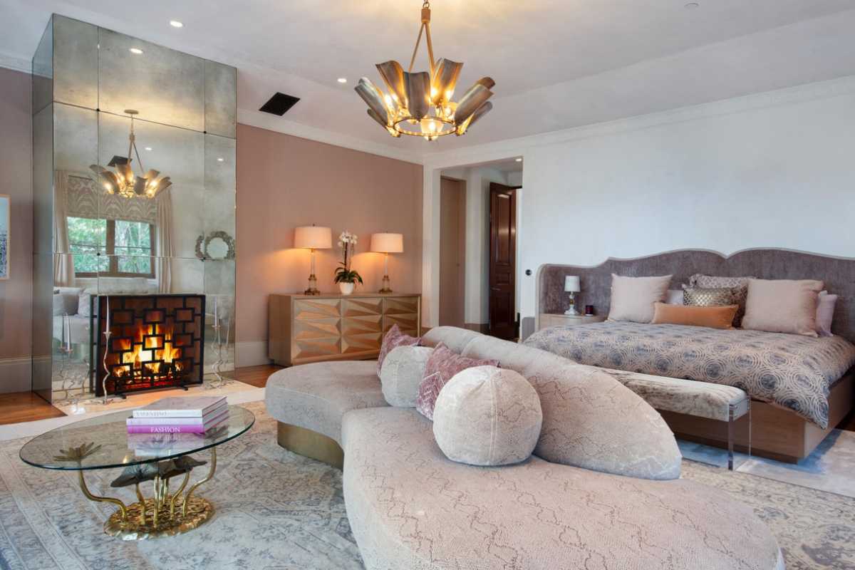 A bedroom with a bed, a fireplace, a white ceiling, a chandelier, a couch, and a coffee table.
