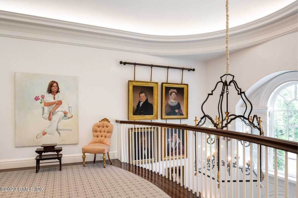 A landing with a wooden floor, rug, white walls, white ceiling, paintings, and a chair.