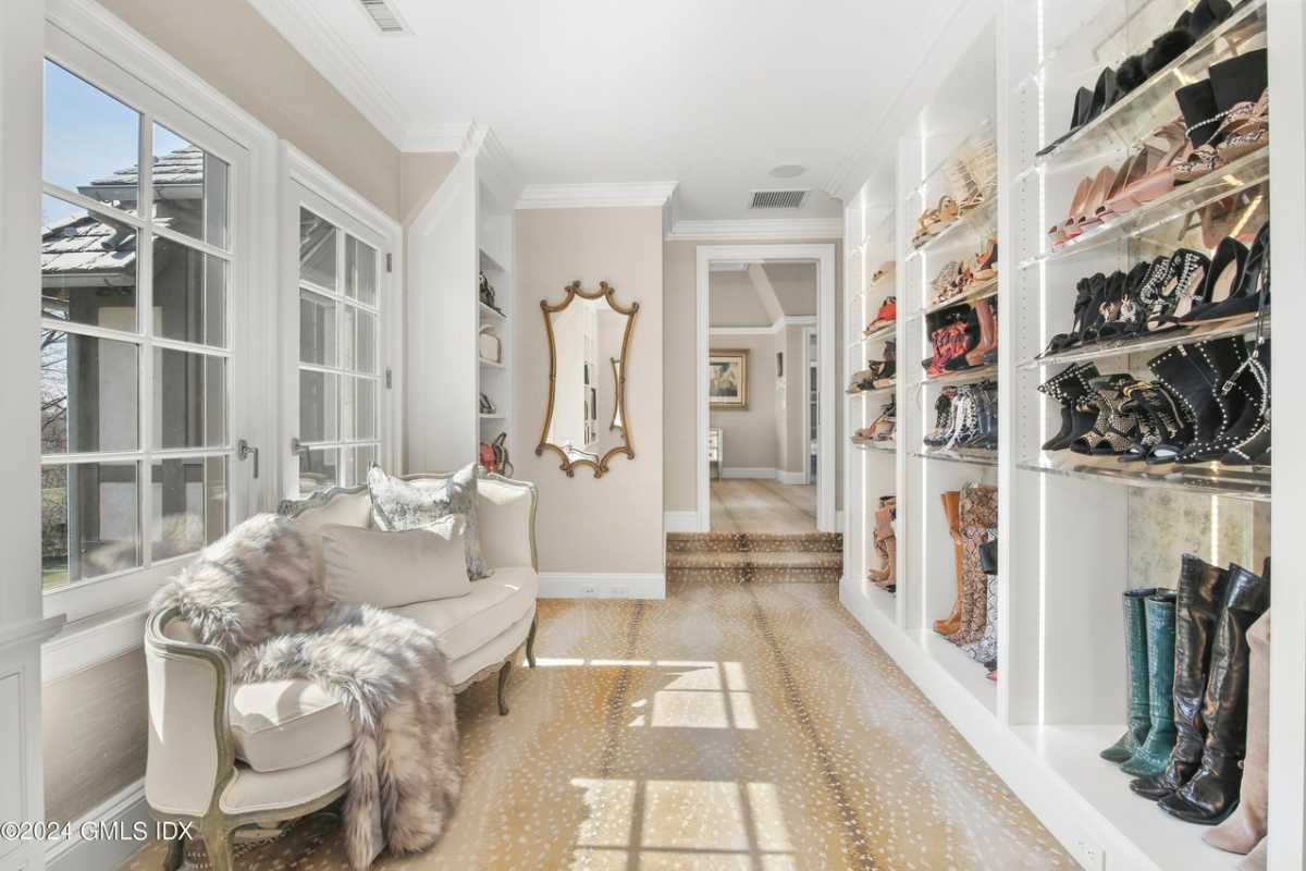 A walk-in closet with a window, a couch, a white ceiling, a mirror, and white shelves.