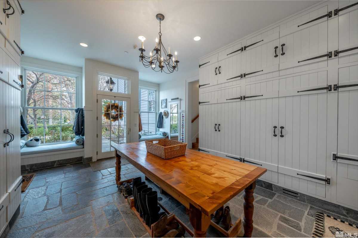 A mudroom with a stone floor, table, windows, chandelier, white ceiling, and white cabinets.