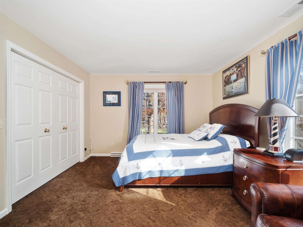 Bedroom with a large bed, glass windows, wooden doors and carpet flooring.