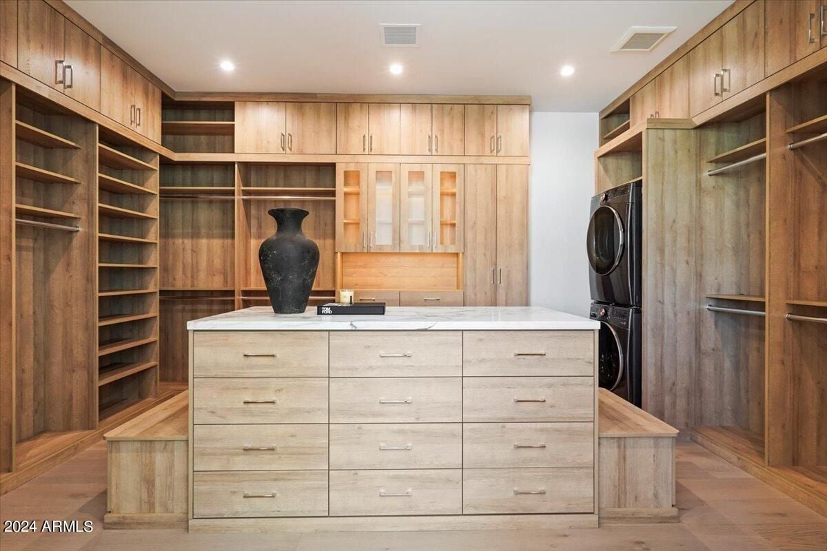 A walk-in closet with a wooden center island, wooden floor, vase, white ceiling, and wooden cabinets.