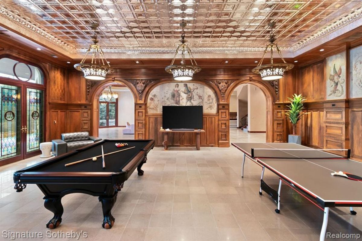A game room with a pool table, pingpong table, a chandelier, and a TV.