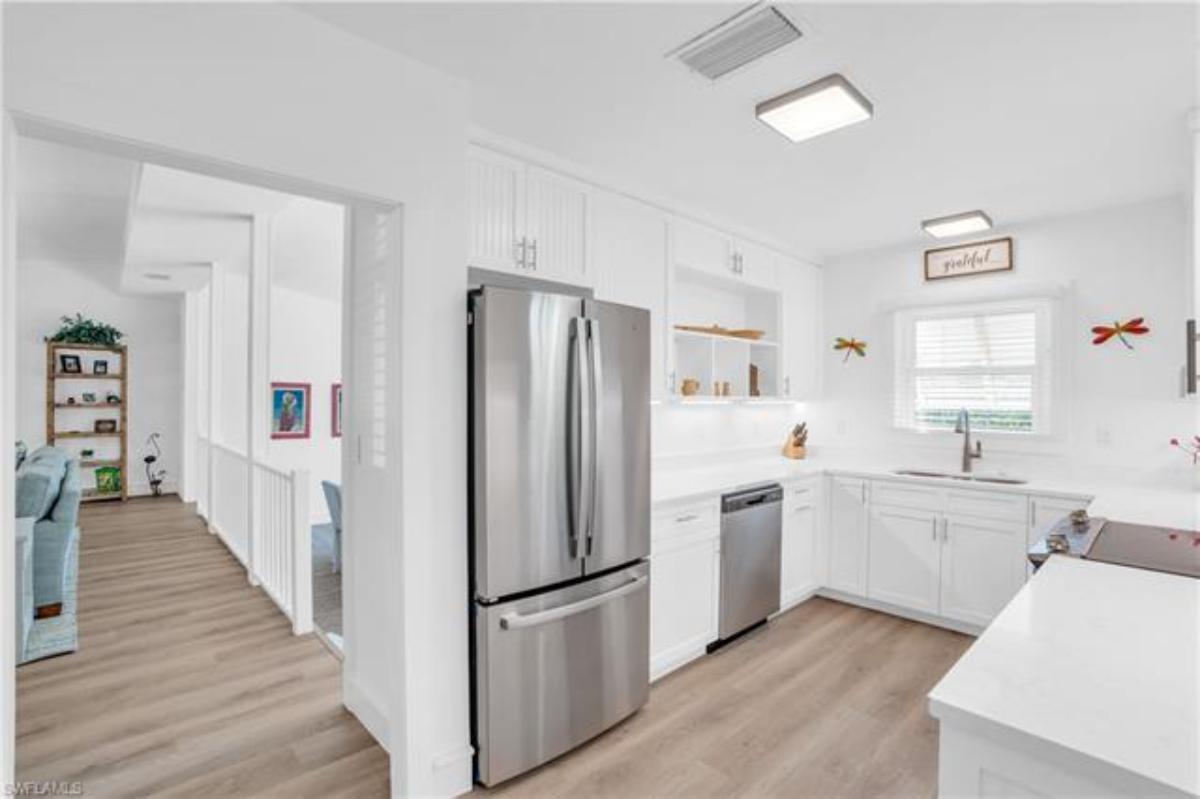 Kitchen with a large island, wooden floor, refrigerator and white custom cabinets.
