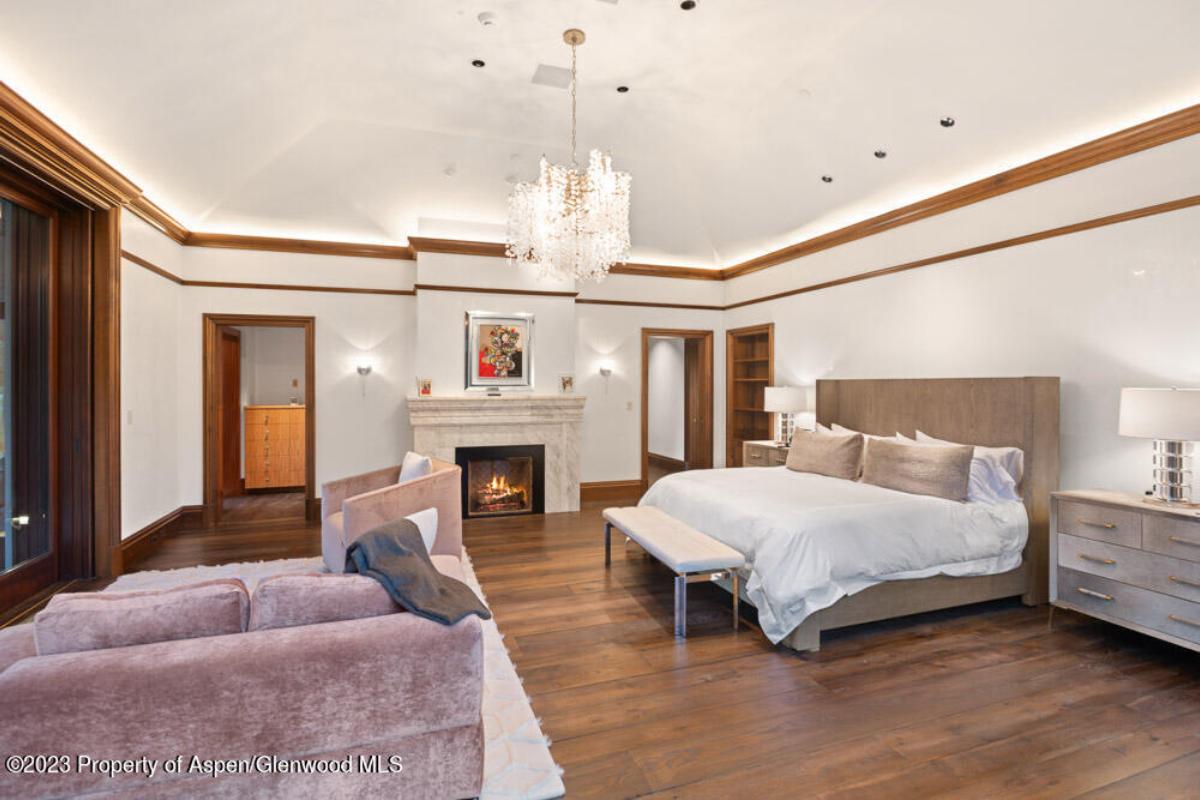 Bedroom with a large bed, chandelier, fireplace and a wooden floor.