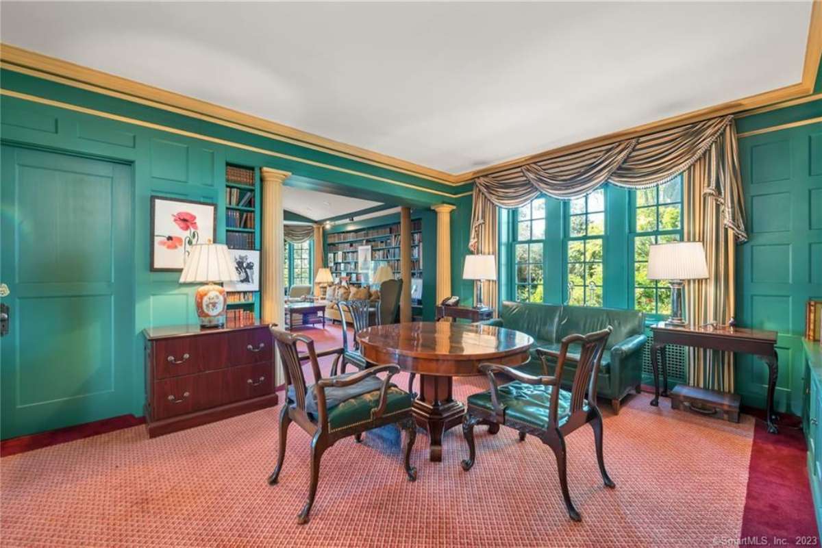 A breakfast nook with a red floor, green walls, windows, a white ceiling, and a round table surrounded by chairs.
