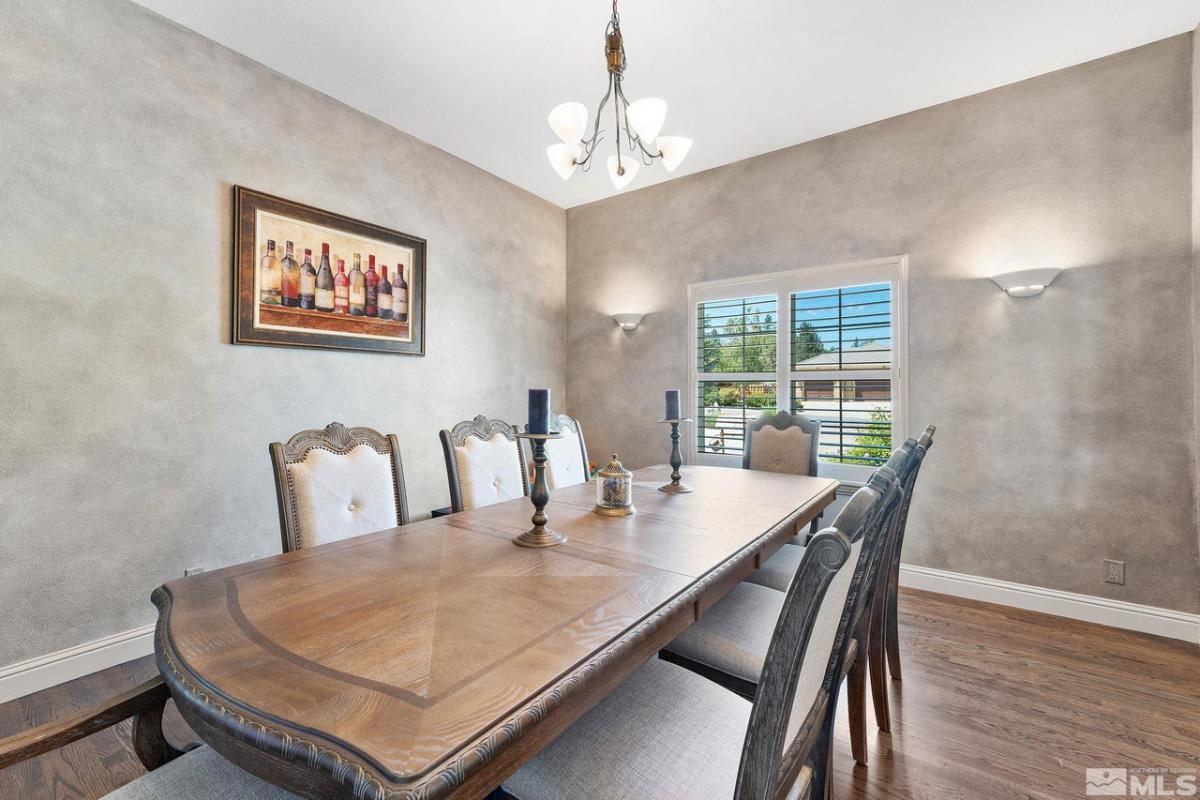 Dining room with a large wooden table, chairs, chandelier and a wood flooring.