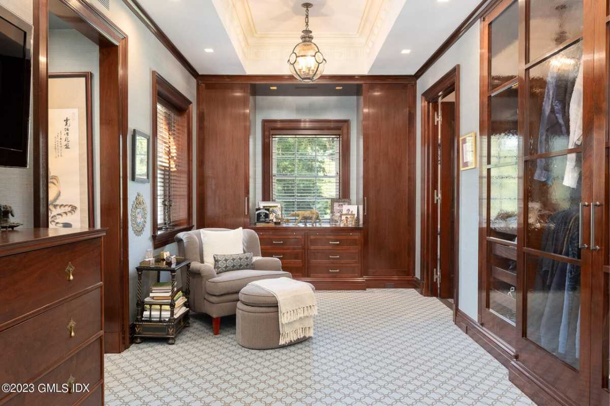 A seating area with a rug, white ceiling, chandelier, wooden cabinets, and a window.