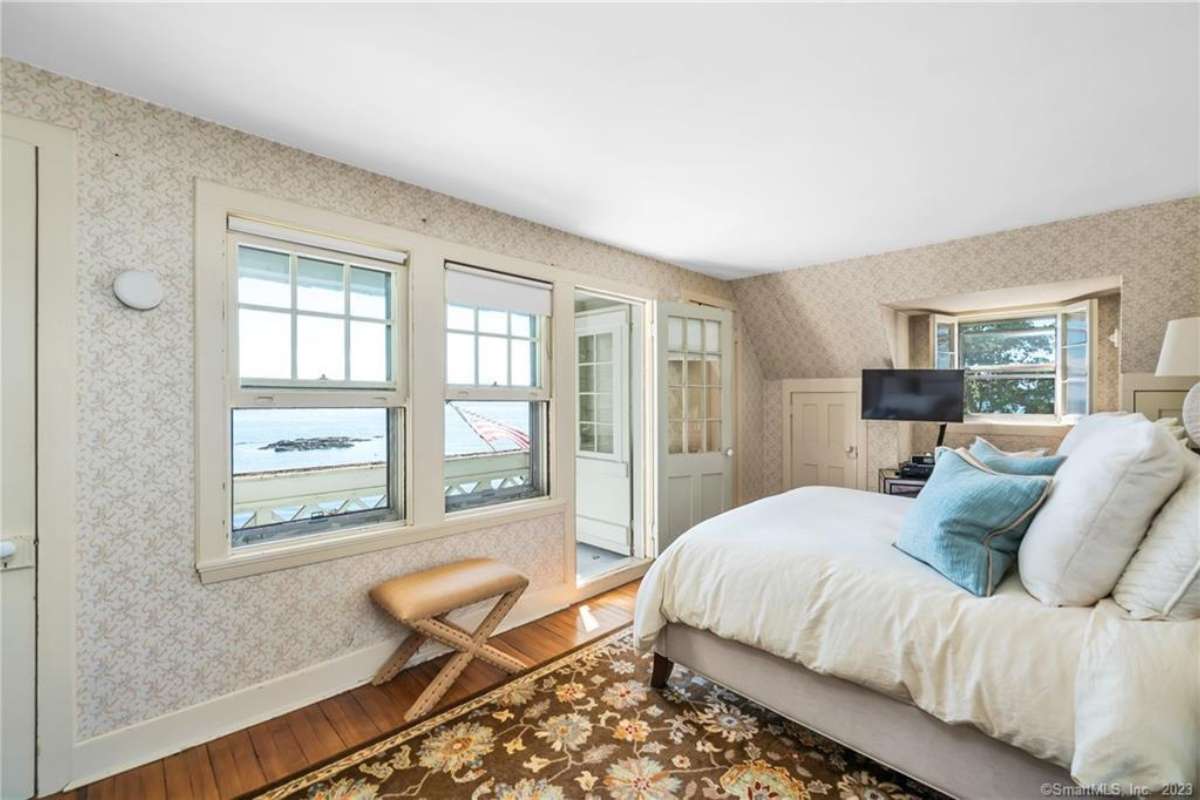 A bedroom with a bed, a rug, wallpaper, a window, a white ceiling, and a TV.