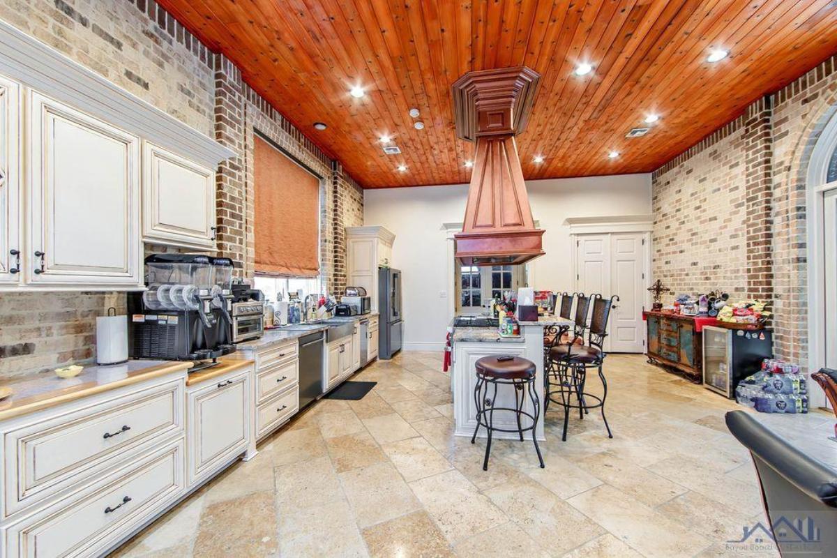 Kitchen with a large island, stove, custom lights and a wooden ceiling.