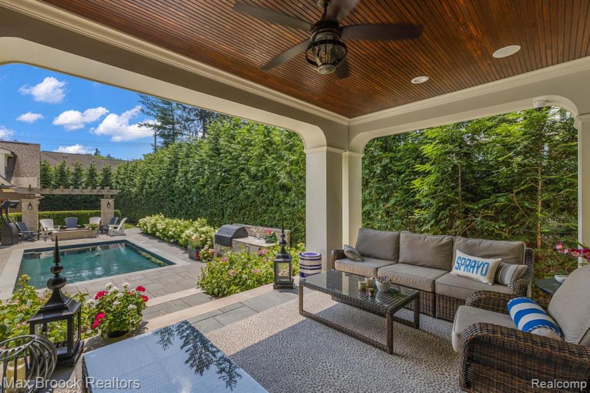 Covered patio with a couch, chair and a pool.