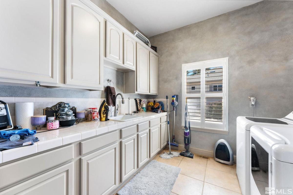 Laundry room with white cabinets, sink, tile flooring, washer and dryer.