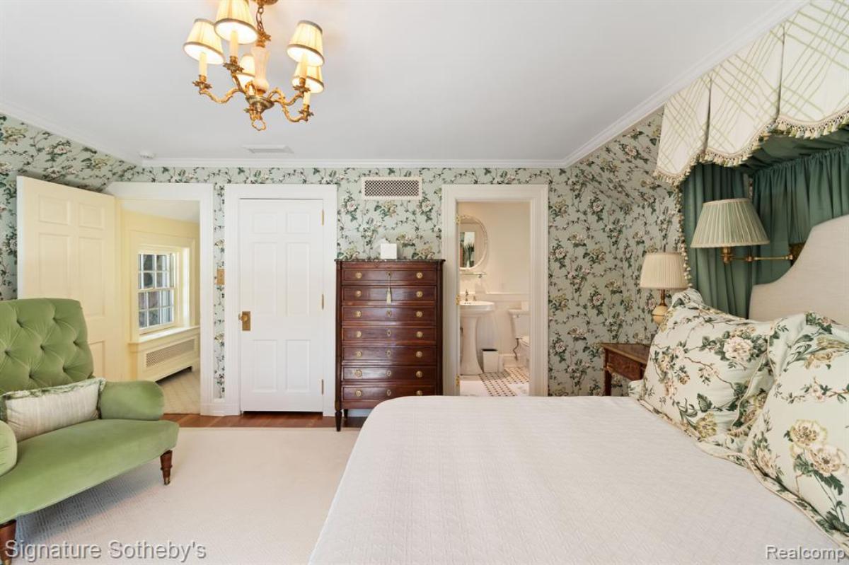 Bedroom with a large bed, couch, large rug and a chandelier.