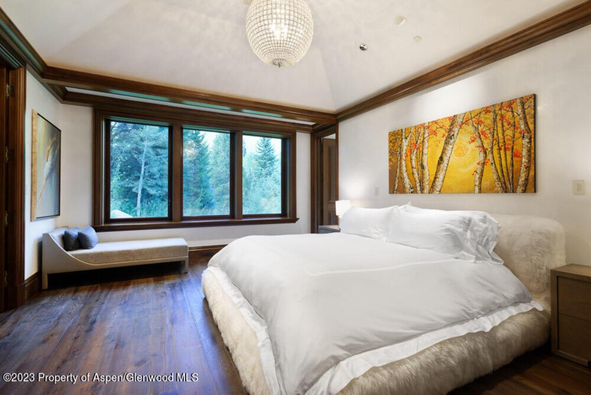 Bedroom with a large bed, chandelier, glass doors and a wooden floor.