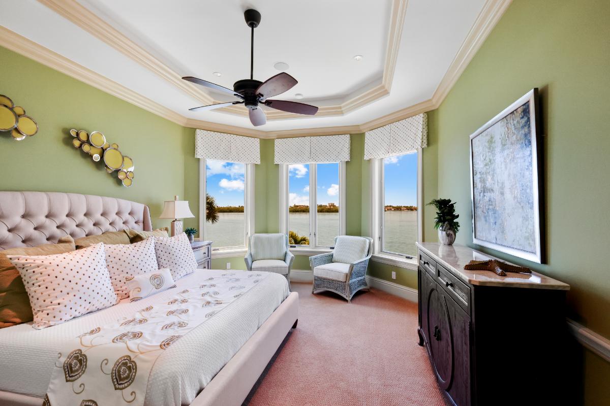 Bedroom with a large bed, carpet flooring and large glass windows overlooking the water.