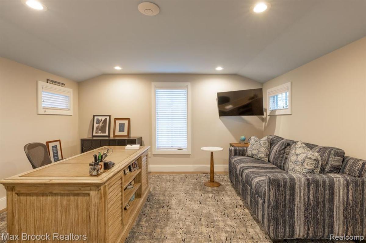 Home office with a desk, TV, couch and a carpet flooring.
