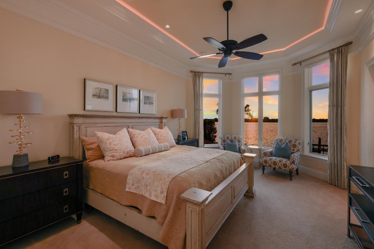Bedroom with a large bed, carpet flooring and large glass windows overlooking the water.