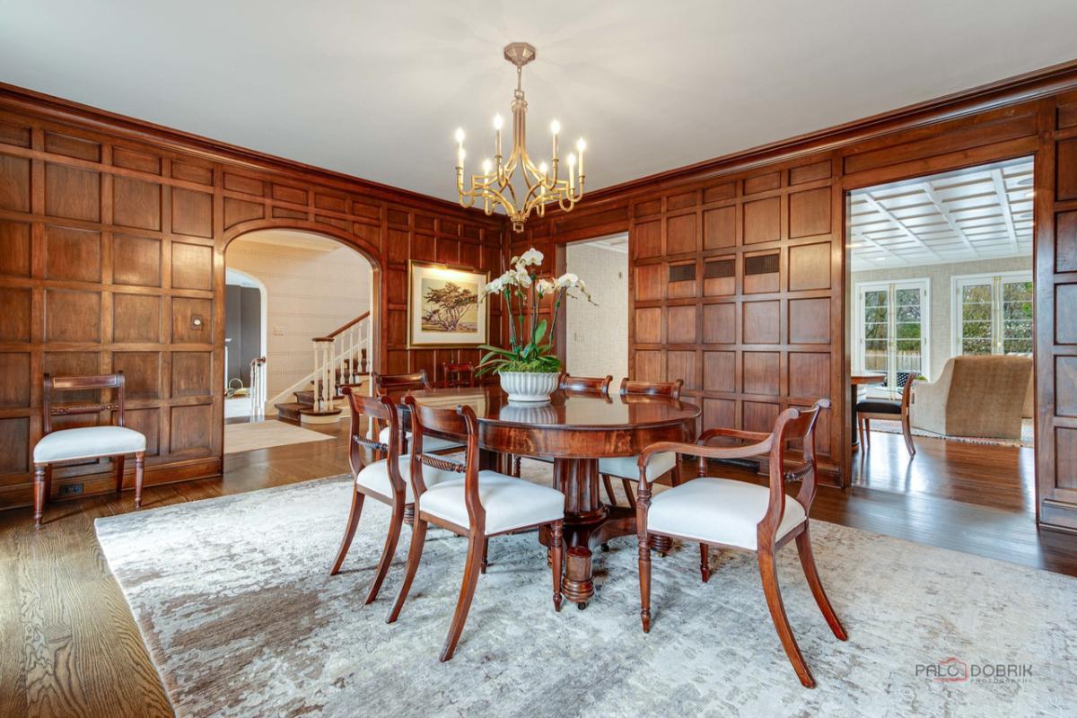 Dining room with a round table, chairs, chandelier, large rug and wood flooring.
