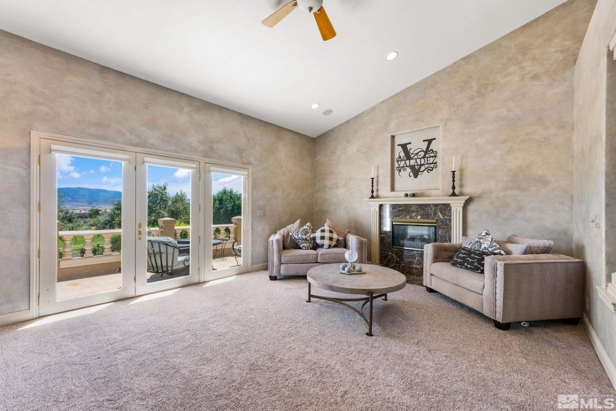 Living room with couches, glass doors, fireplace and a carpet flooring.